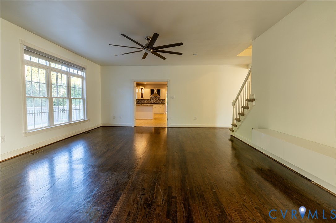 Open-concept interior featuring dark-stained wood-finish flooring, a multi-blade ceiling fan, expansive multi-pane windows, and a staircase with a white balustrade