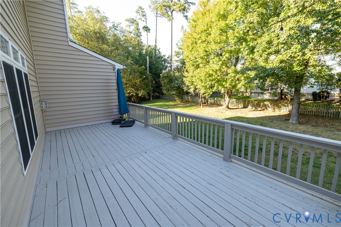 Spacious elevated deck featuring horizontal slat railing, neutral-toned plank decking, vinyl siding, and string lighting