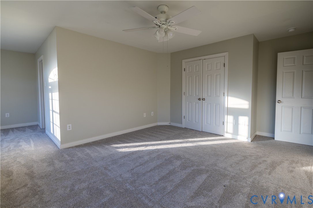 Neutral-toned interior space featuring carpeting, a white ceiling fan with integrated lighting, and dual-panel closet doors
