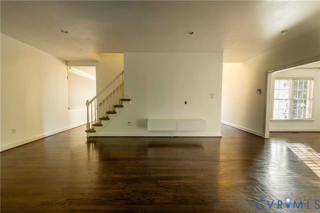 Open floor plan featuring wood-finish flooring, recessed lighting, a white wall-mounted media console, and a staircase with white balusters