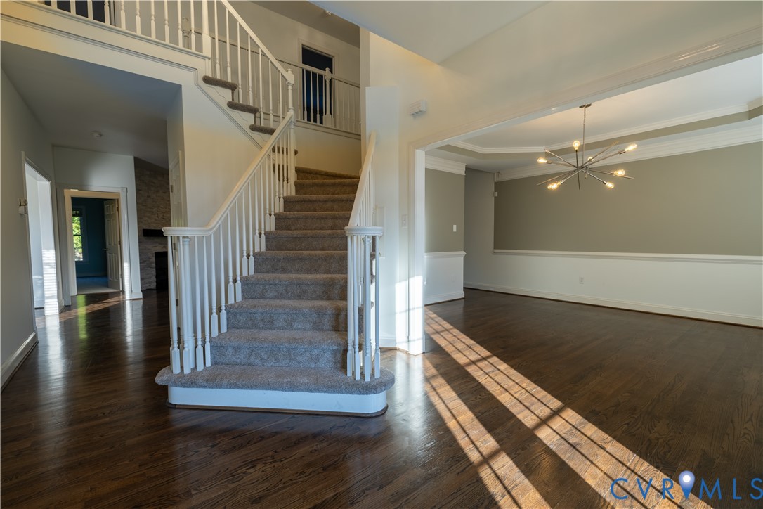 Foyer featuring wood-finish flooring, a staircase with white balusters, crown molding, chair rail trim, and a multi-arm modern chandelier