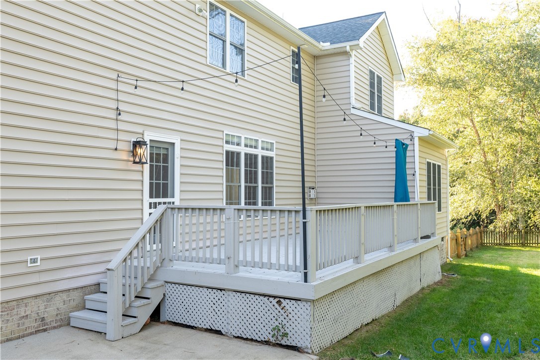 Rear exterior featuring horizontal vinyl siding, a raised deck with painted railings, latticed skirting, and a concrete patio