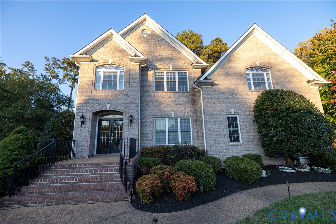 Two-story brick exterior featuring a multi-gabled roofline, double-door entryway, exterior wall-mounted light fixtures, and multi-pane windows