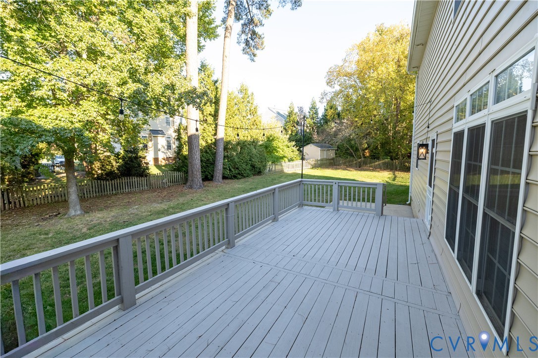 Elevated rear deck featuring light-toned wood-finish decking and perimeter railings, overlooking a fenced backyard with mature trees