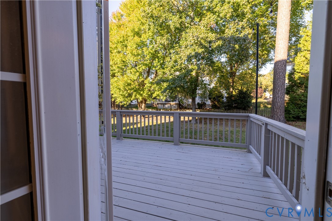 Elevated exterior deck featuring painted wood-finish decking, vertical balustrades, and wood post railings, overlooking a backyard with mature trees