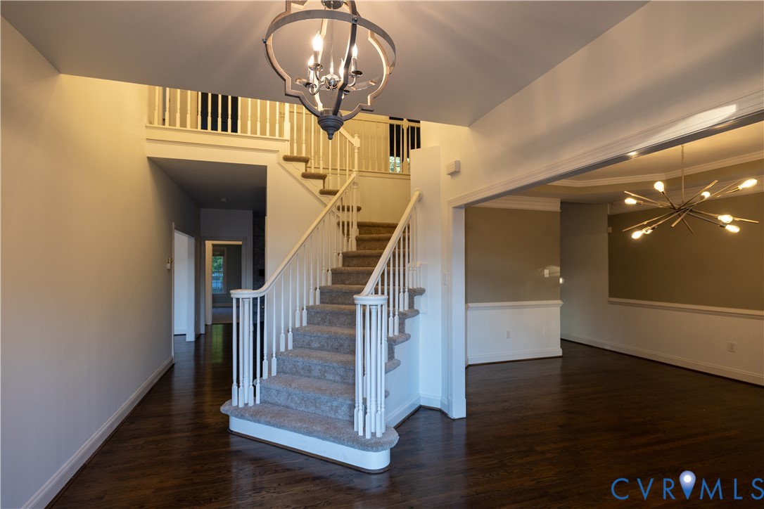 Foyer featuring wood-finish flooring, a two-story staircase with white spindles, a sculptural geometric chandelier, and a tiered mid-century modern style light fixture
