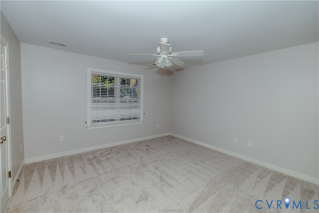 Neutral-toned interior featuring wall-to-wall carpeting, a multi-blade ceiling fan with integrated lighting, and a window with horizontal blinds