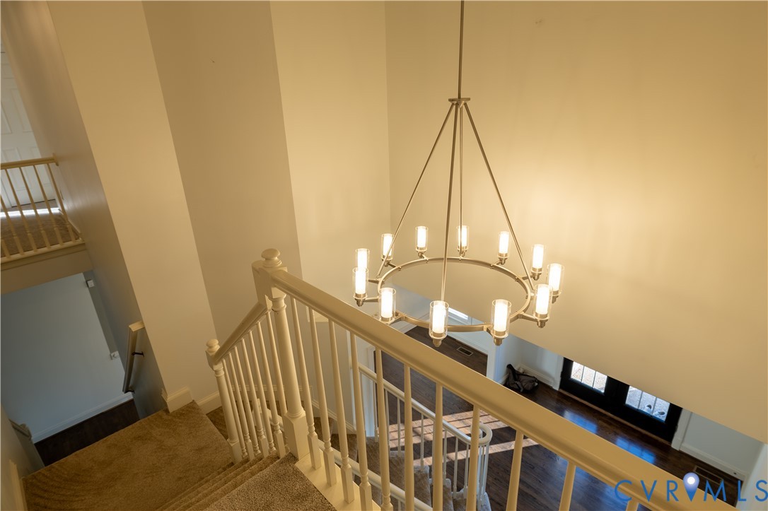 Multi-story foyer featuring a contemporary circular chandelier with twelve cylindrical glass shades, high-reaching walls, and a white balustrade staircase with wood-finish flooring