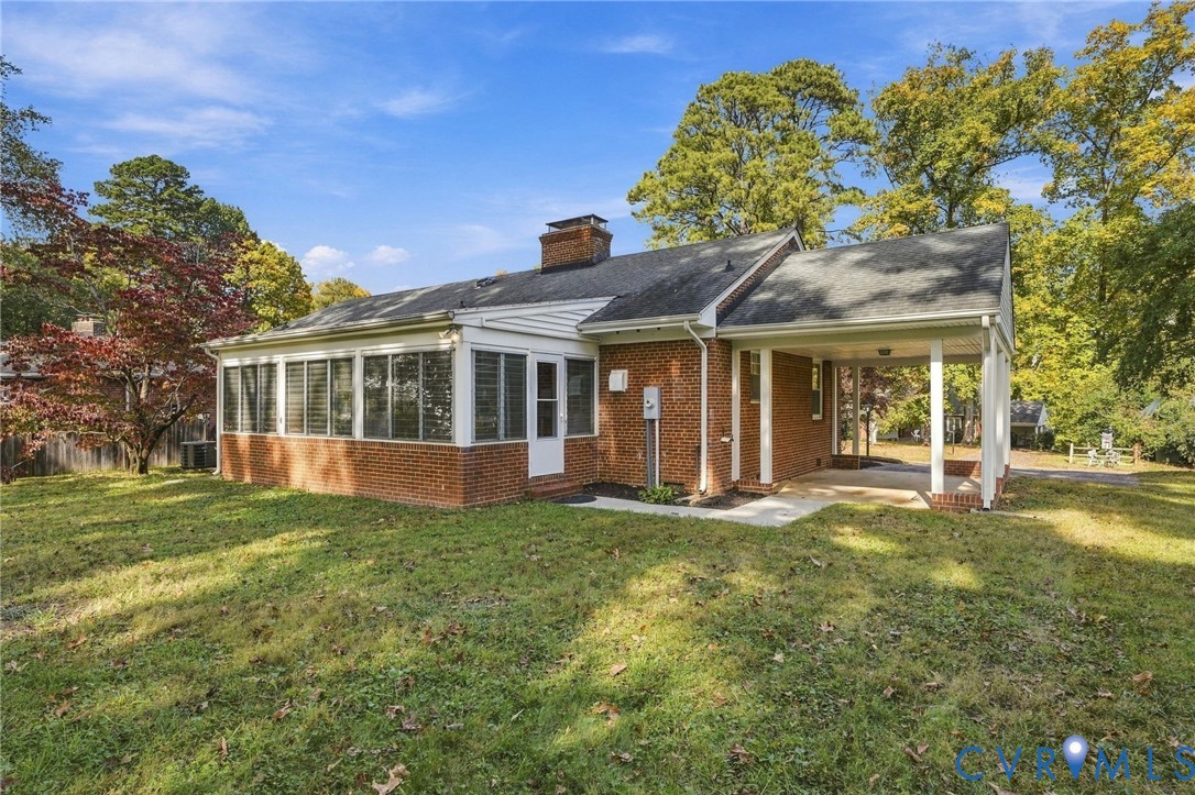 Brick exterior featuring a multi-windowed sunroom, a covered carport, and a masonry chimney
