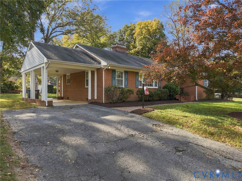 Brick exterior featuring an attached carport, asphalt driveway, chimney, and multi-pane windows with shutters