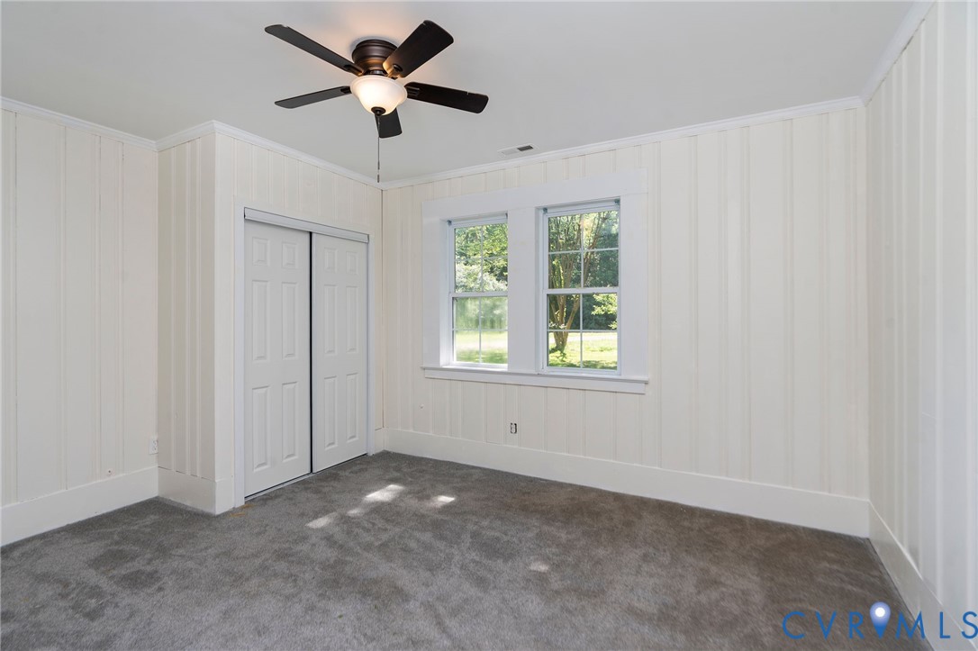 Room featuring vertical paneled walls, neutral carpet, double-hung windows, and a ceiling-mounted light fixture with integrated fan