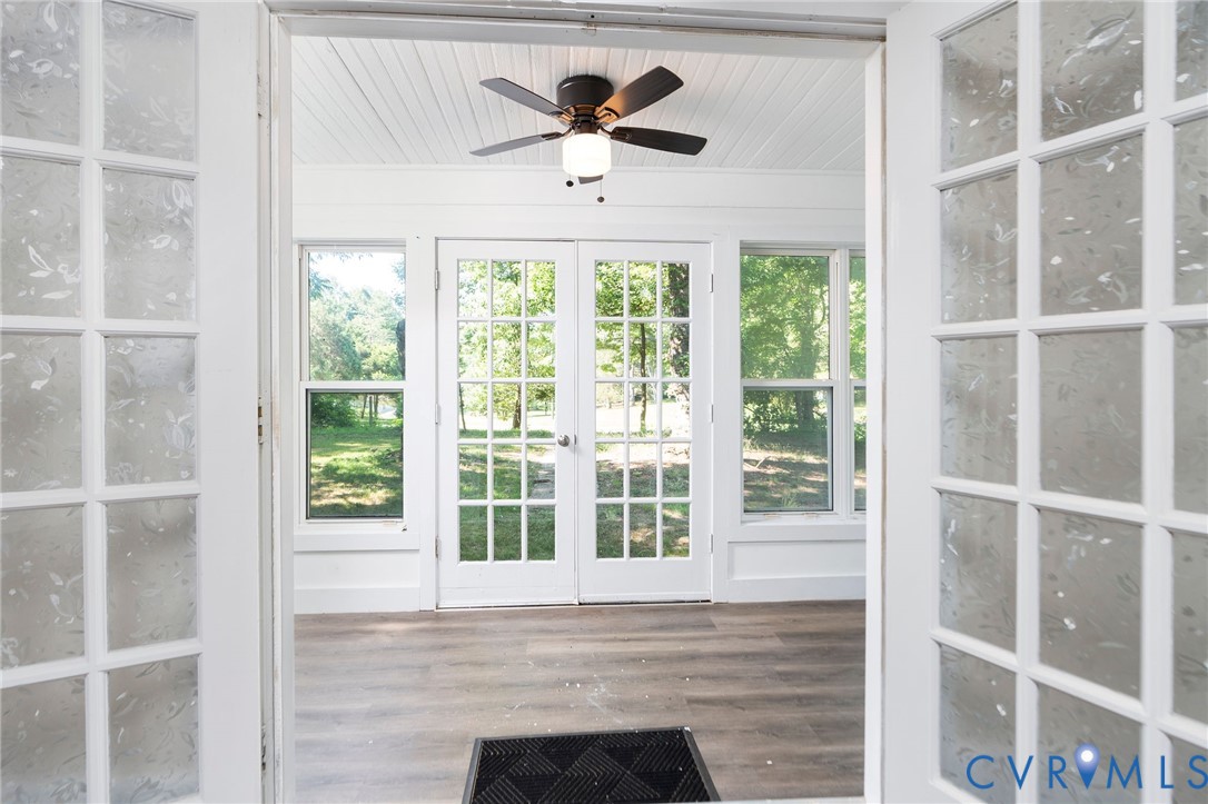 Sunroom featuring wood-finish flooring, white beadboard ceiling, ceiling fan with integrated lighting, and multiple French doors with glass panes