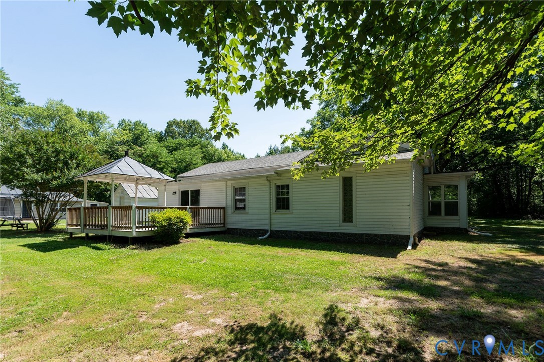 Backyard featuring a raised wooden deck with a gazebo, white siding, and mature trees