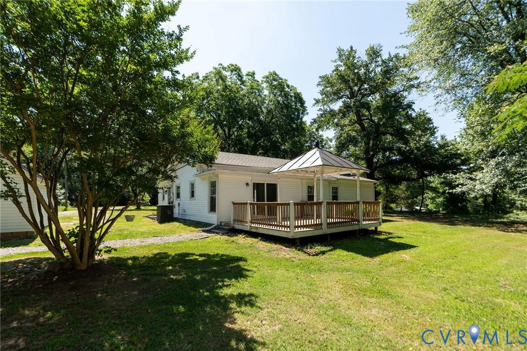 Rear exterior featuring a wood deck, metal-roofed gazebo, siding, and mature trees on a lawn