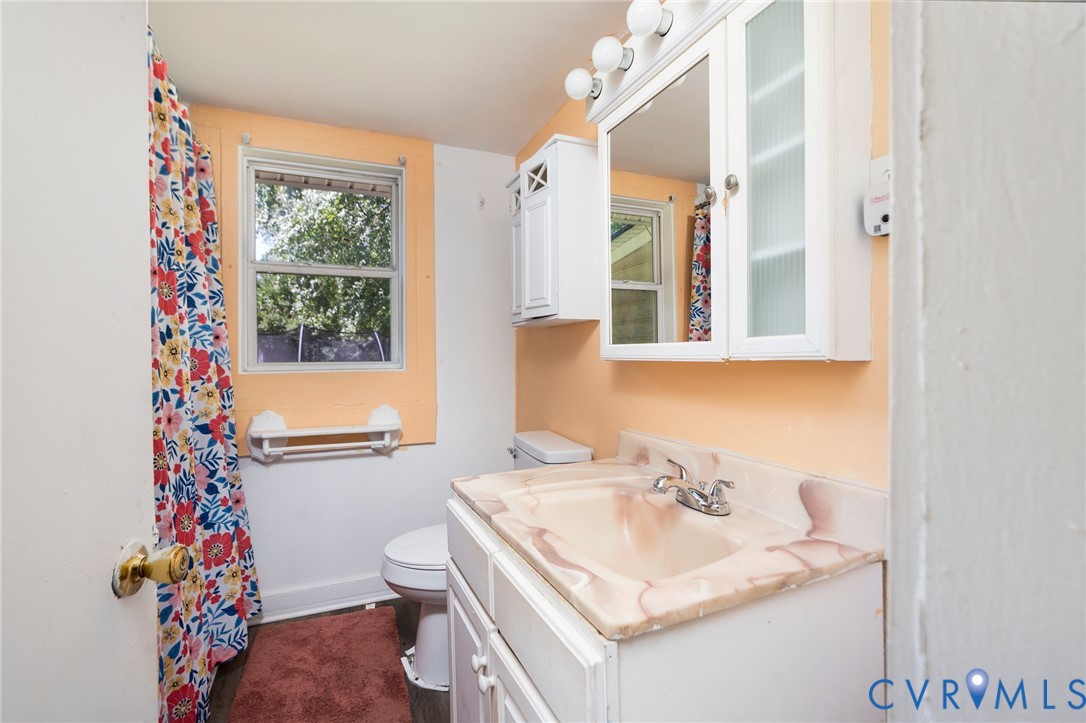 Bathroom featuring a white vanity cabinet with an integrated sink and countertop, a wall-mounted medicine cabinet with integrated lighting, and a single-pane window