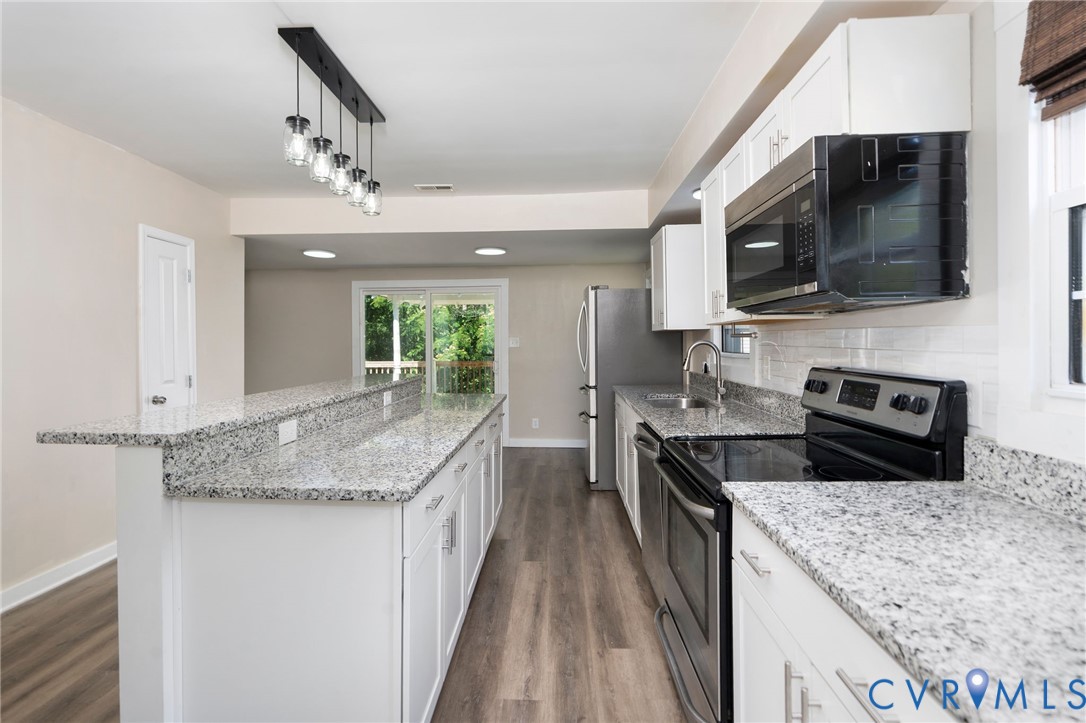 Kitchen featuring white cabinetry, stone countertops, stainless steel appliances, a multi-pendant light fixture, and wood-finish flooring
