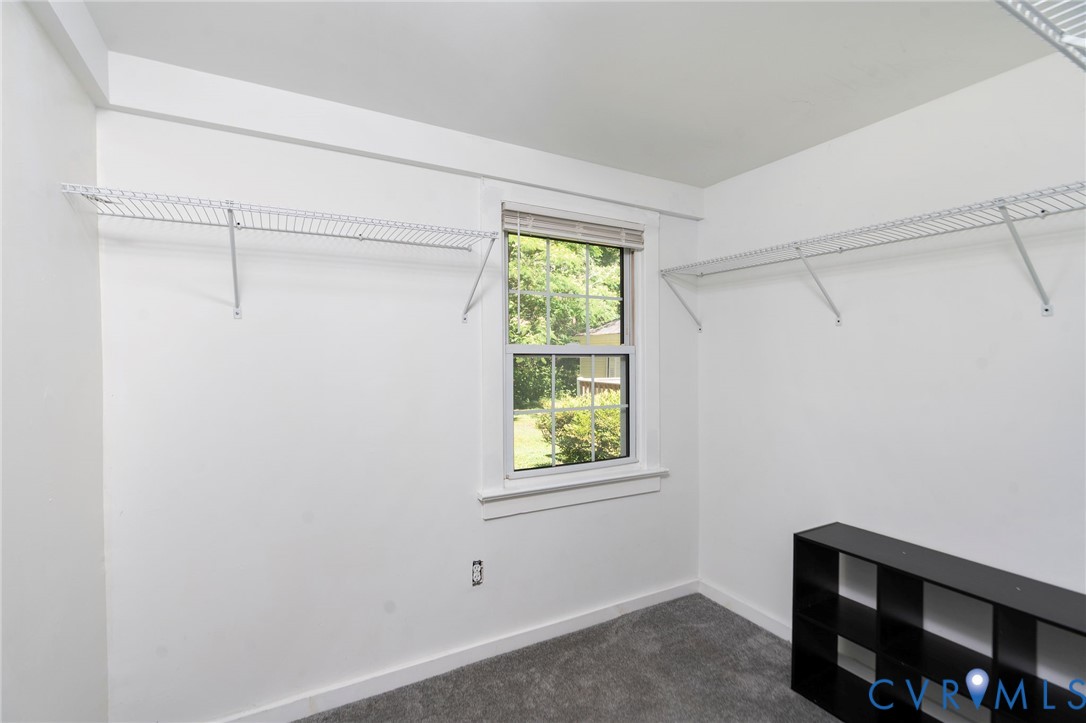 Storage space featuring dual wall-mounted white wire shelving units, a double-hung window with a wood-trimmed frame, and neutral carpeting