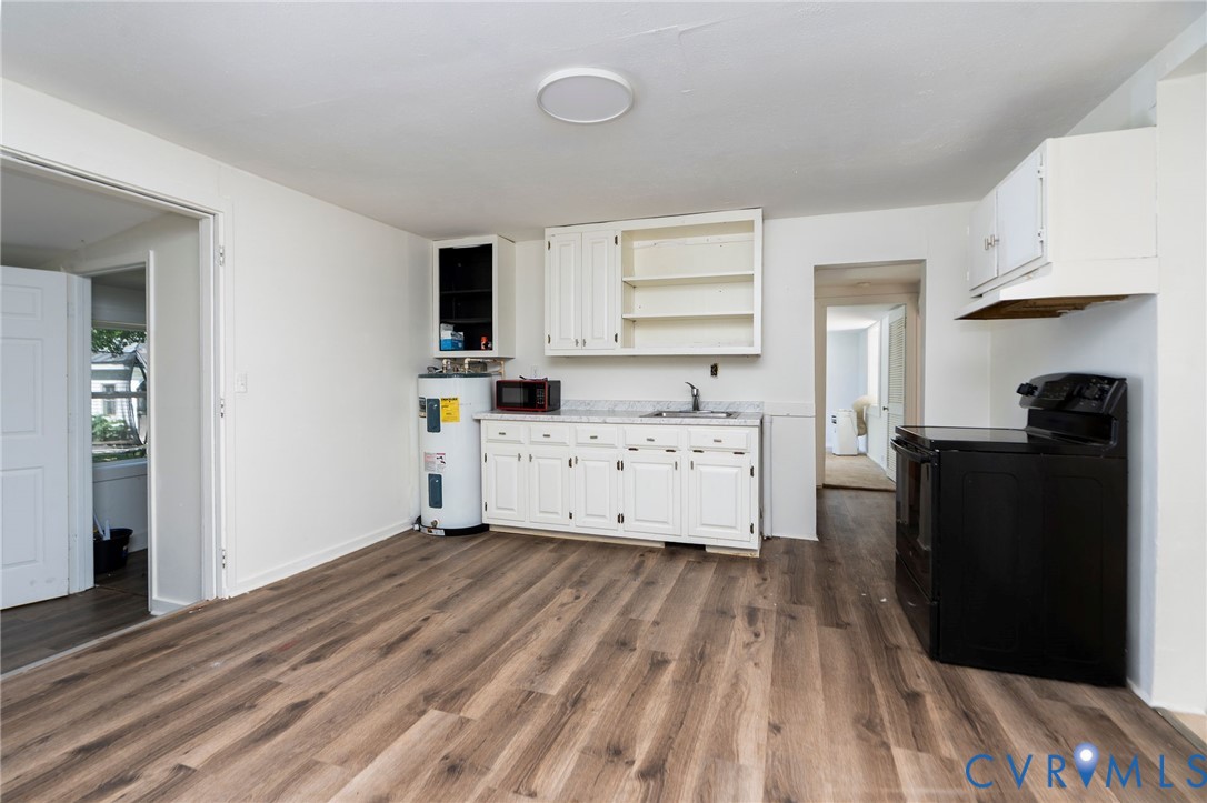 Kitchen featuring wood-finish flooring, white cabinetry, light-toned countertop, and black range