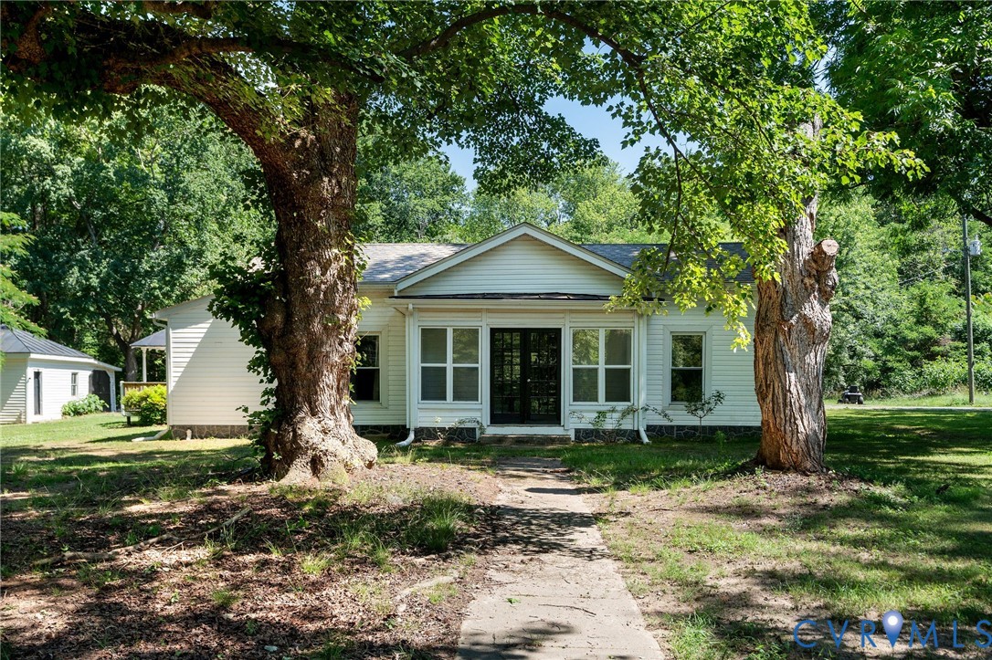 Single-story exterior featuring white horizontal siding, a central gable roofline, multi-pane glass entry doors, and mature trees
