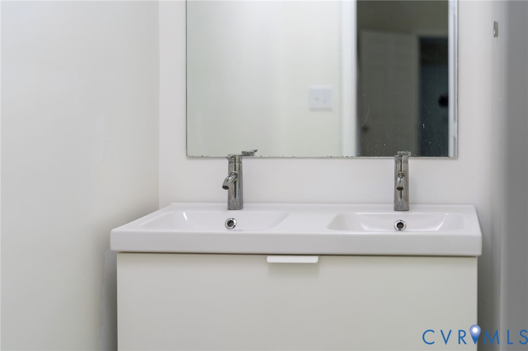 Double-sink vanity featuring a white cabinet base, integrated dual-basin countertop, chrome faucets, and a wall-mounted mirror