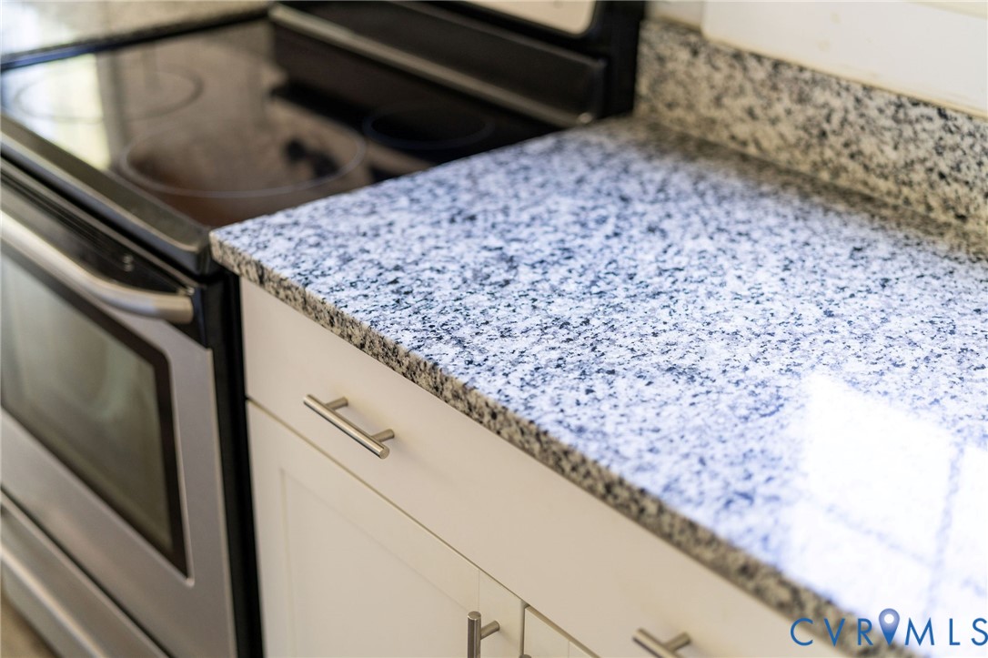 Stone-surface countertops, white cabinetry with metallic pulls, and stainless steel smooth-top range