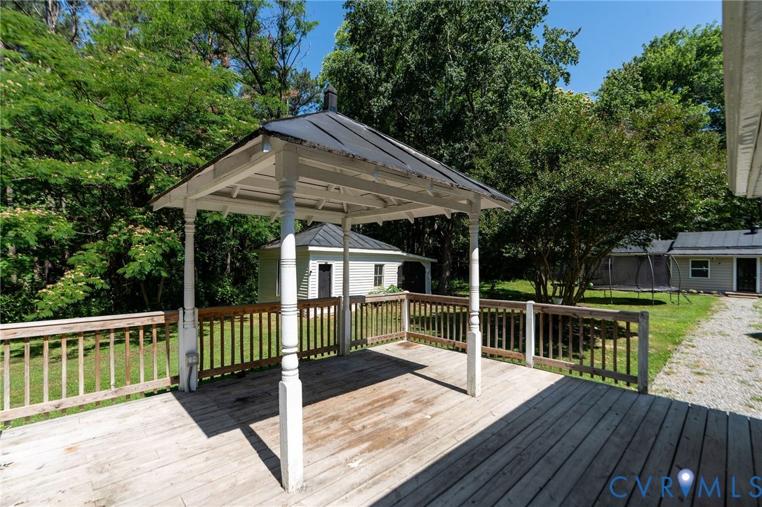 Elevated wood deck featuring a covered gazebo with a metal roof and painted wooden support columns, bordered by a wooden railing