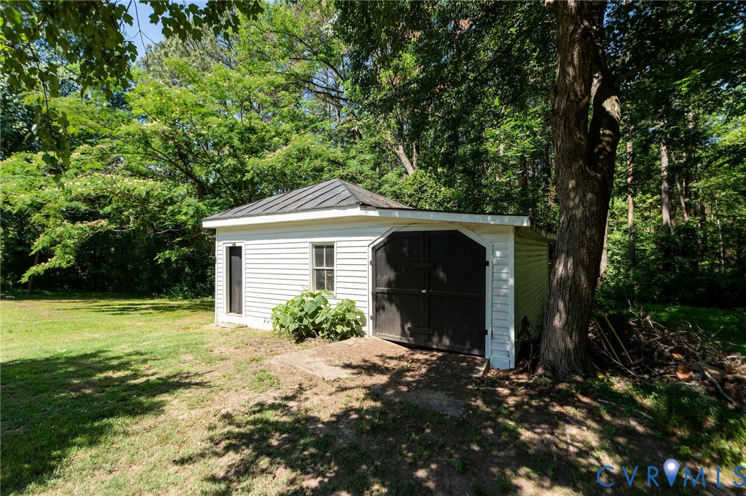 Detached garage with horizontal siding, a metal roof, and arched double doors, situated on a lot with mature trees