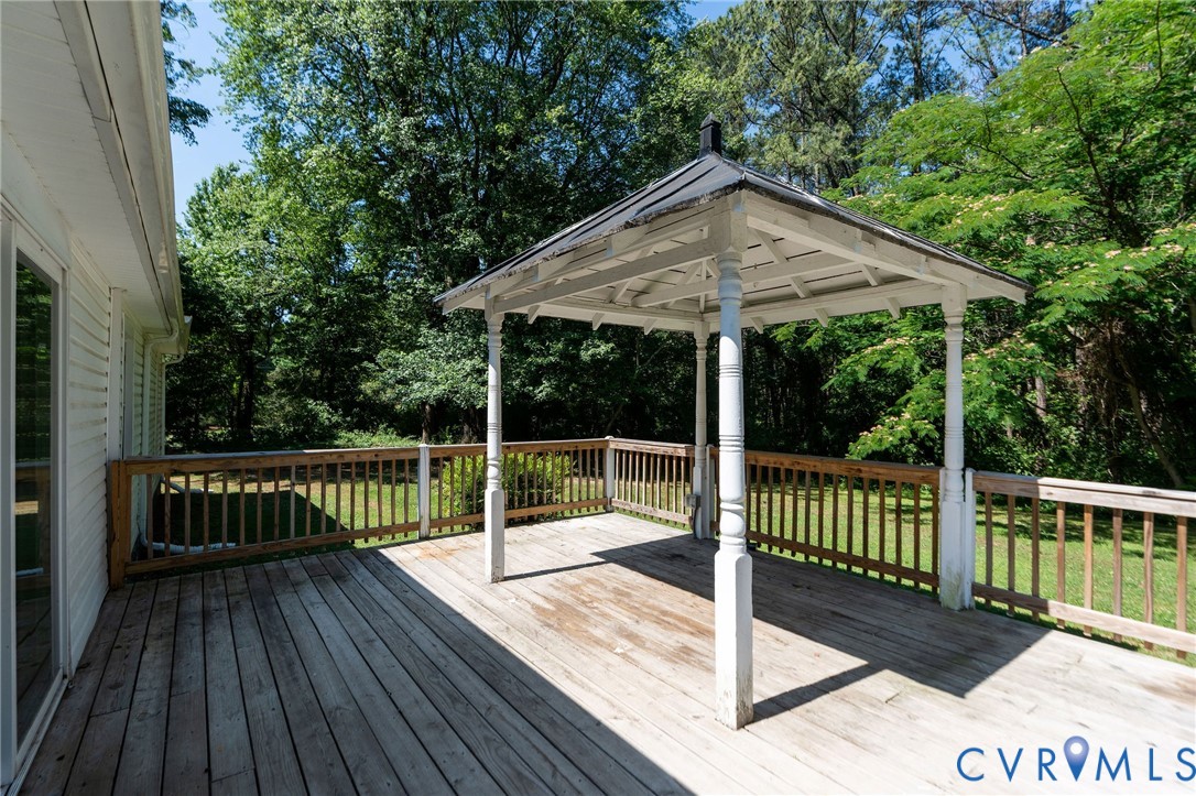 Outdoor wooden deck featuring a covered gazebo, wooden railings, and mature surrounding trees