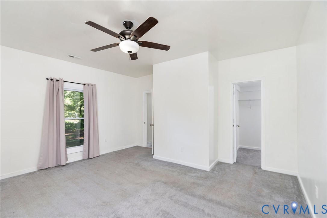 Room featuring neutral-toned carpeting, a ceiling fan with integrated lighting, and a walk-in closet