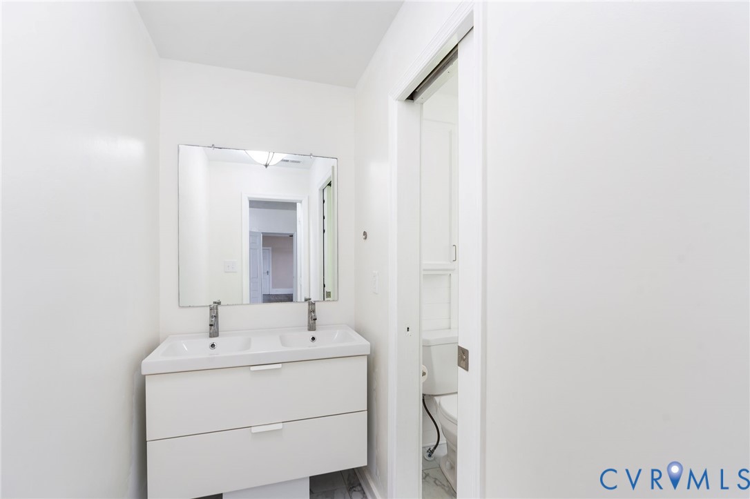 Floating double vanity featuring a white composite countertop, integrated dual sinks, chrome faucets, and two storage drawers, paired with a frameless rectangular mirror and sliding door entry