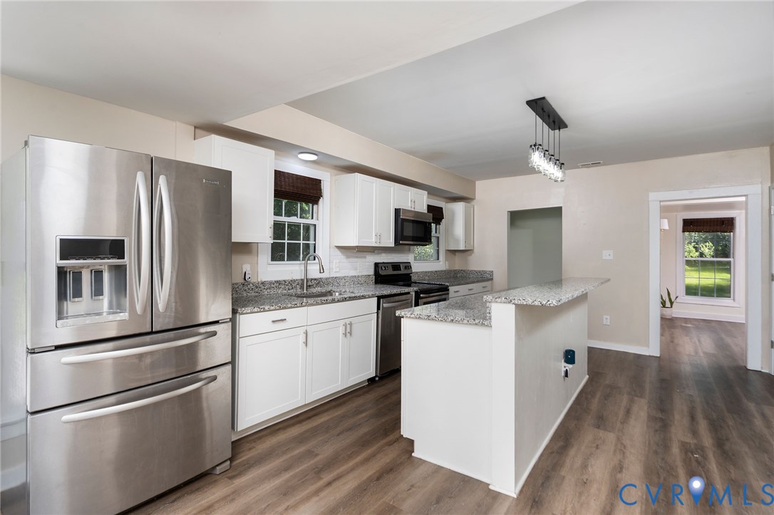 Kitchen featuring white shaker-style cabinetry, stone-finish countertops, stainless steel appliances, a peninsula counter, and wood-finish flooring