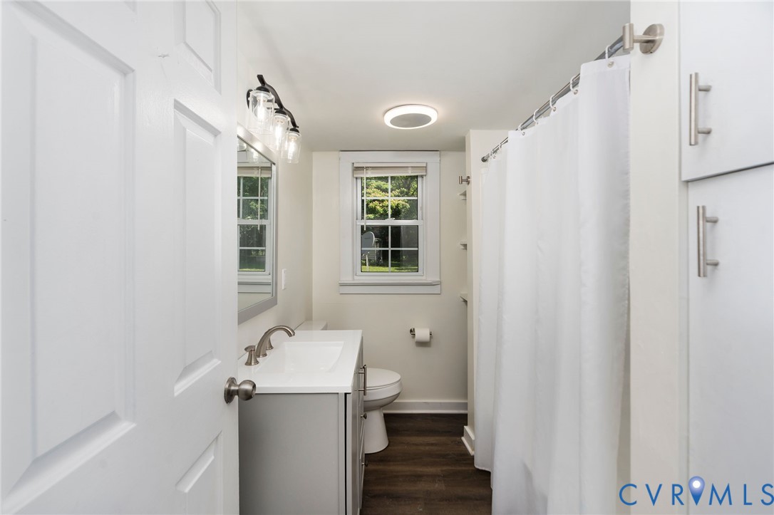 Bathroom featuring a vanity with a white countertop and basin, wood-finish flooring, built-in cabinetry, and multi-light vanity fixture