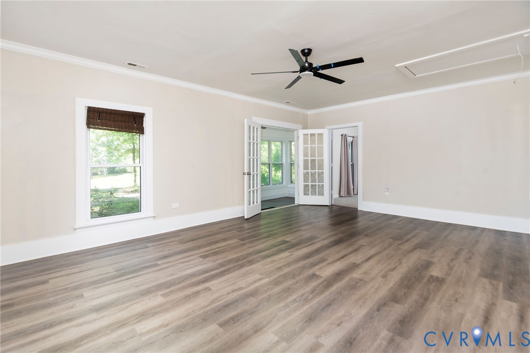 Wood-finish flooring, crown molding, double French doors, ceiling fan with integrated lighting, and multi-pane window