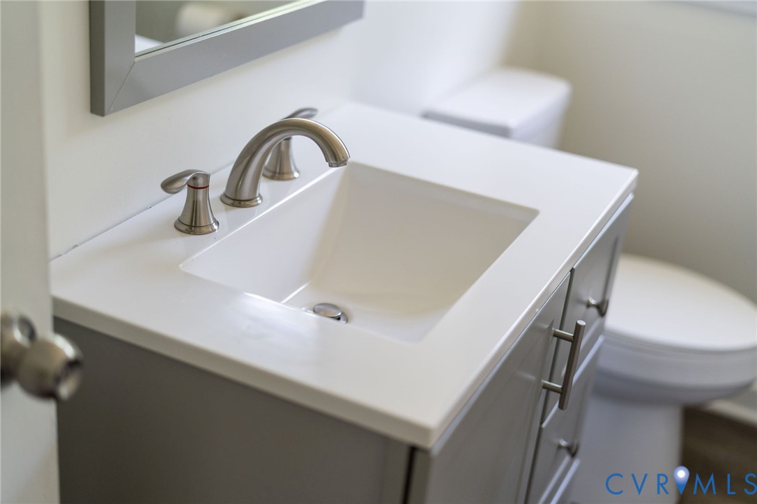 Grey vanity cabinet featuring a white countertop with an integrated rectangular basin, brushed-nickel widespread faucet, and metal hardware