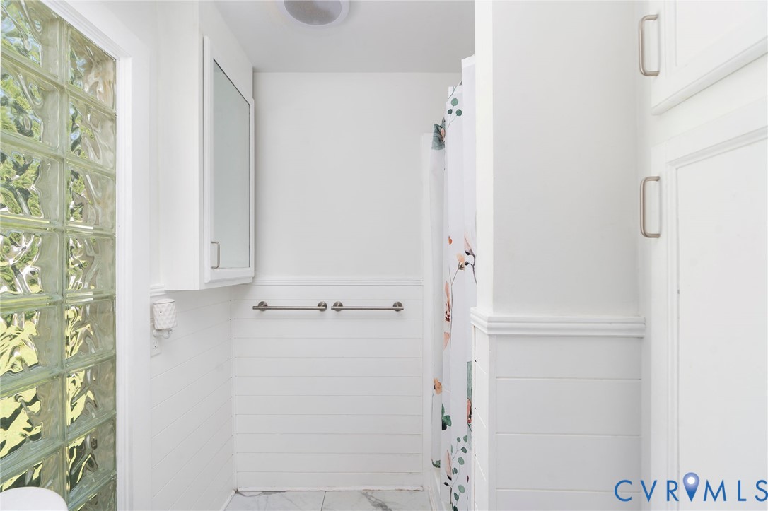 Bathroom featuring glass block accent wall, white horizontal wall paneling, built-in medicine cabinet, and metal hardware