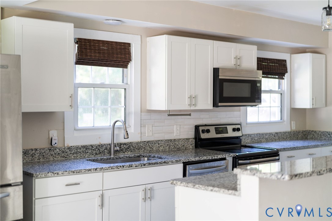 Kitchen featuring white shaker-style cabinetry, speckled stone-finish countertops, white subway tile backsplash, stainless steel appliances, and a gooseneck faucet