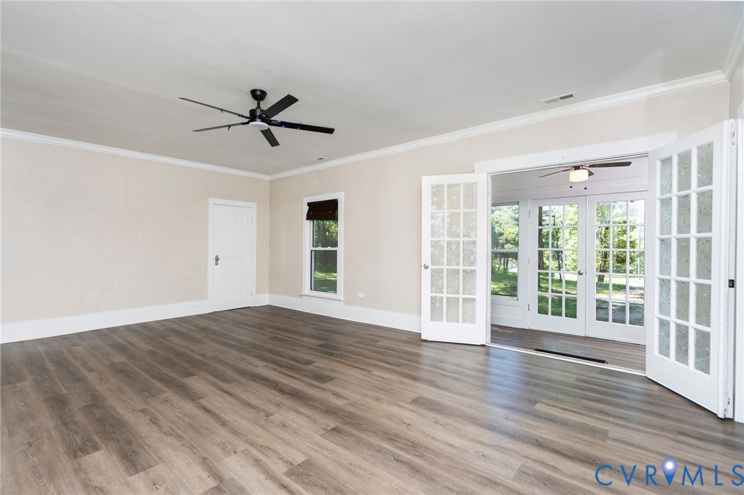 Interior space featuring wood-finish flooring, white French doors, crown molding, and a multi-blade ceiling fan