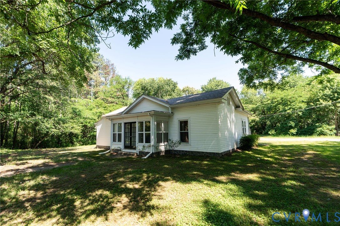 Exterior featuring white horizontal siding, gable roofline, multi-pane glass entry doors, and a natural tree canopy setting