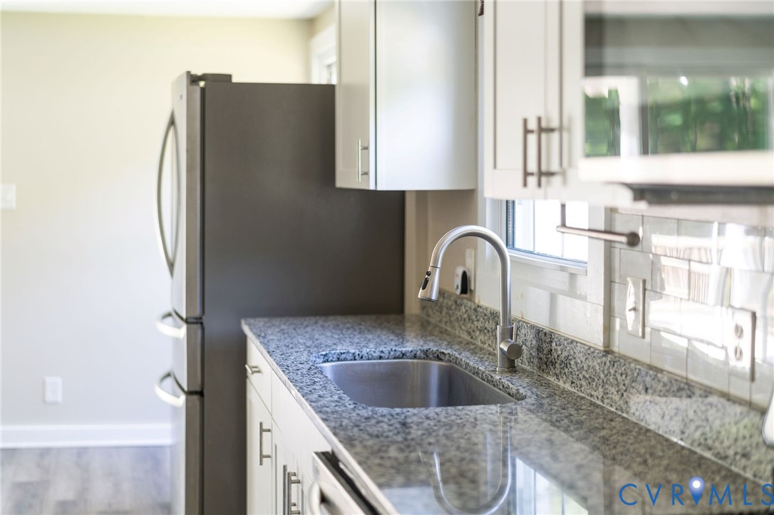 Kitchen featuring white shaker-style cabinetry, stone countertops, undermount stainless steel sink, pull-down faucet, and light-toned wood-finish flooring