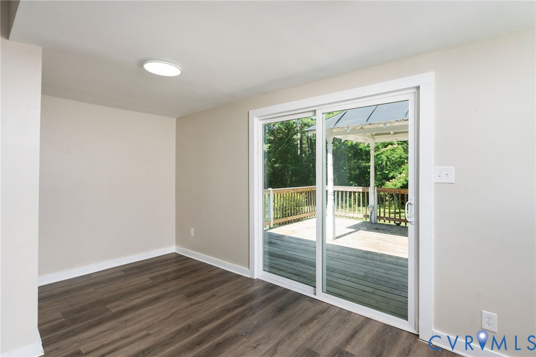 Interior space featuring wood-finish flooring, neutral wall paint, flush-mount ceiling lighting, and sliding glass doors providing outdoor access to a wood deck with a gazebo