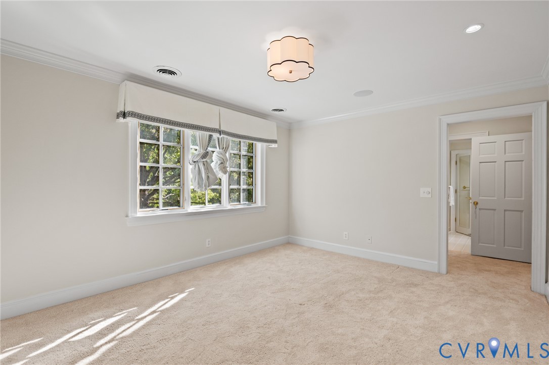 Multi-pane window with detailed molding, crown molding, scalloped flush-mount lighting fixture, neutral wall-to-wall carpeting, and six-panel interior door