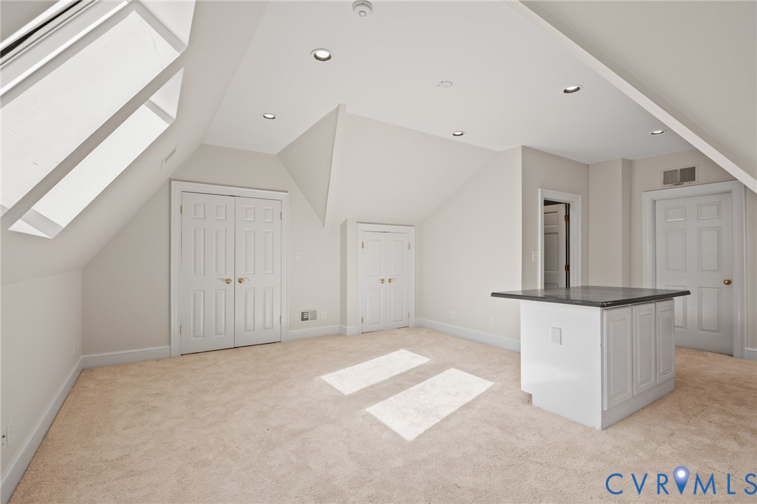 Vaulted ceilings with recessed lighting, skylights, dual closet configurations, and a built-in island with a dark stone-finish countertop