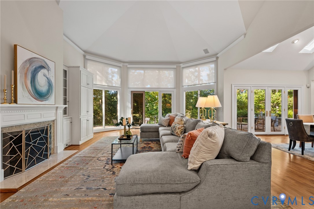 Vaulted ceilings, fireplace with custom geometric metal screen, built-in cabinetry, wood-finish flooring, and expansive windows