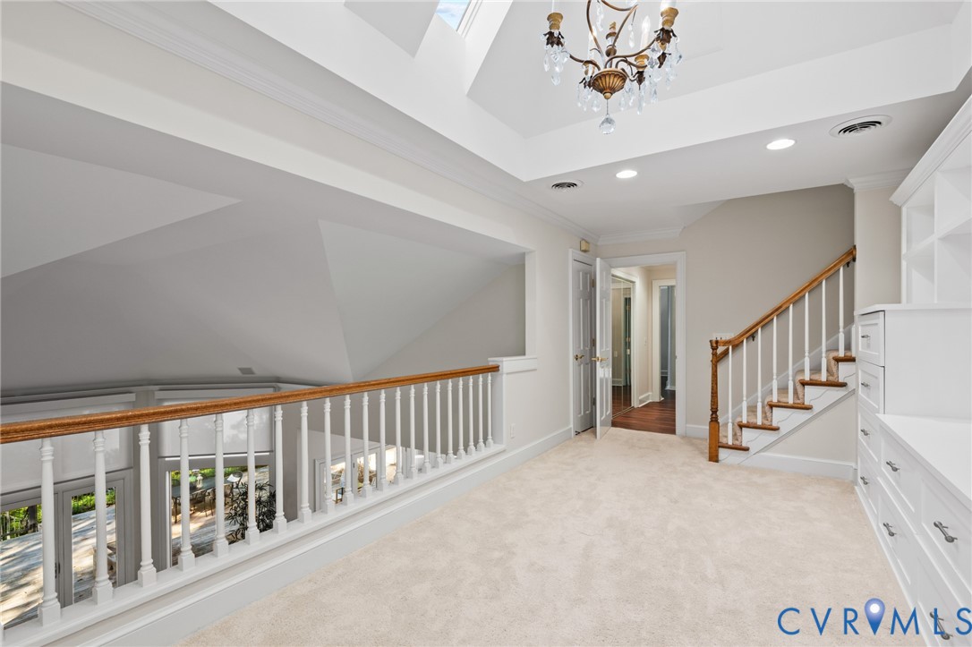 Vaulted ceiling with skylight, custom built-in cabinetry, decorative chandelier, and wood-railed staircase