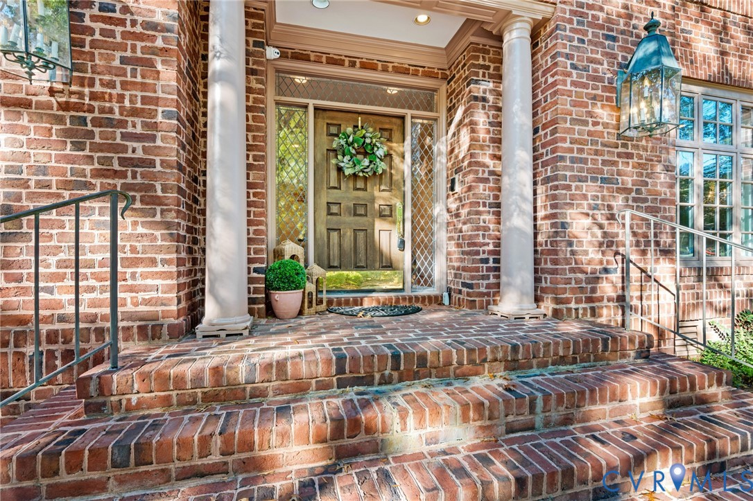 Classic brick exterior featuring a multi-step brick entryway, dual architectural columns, side-light windows with patterned detailing, and metal-cased carriage-style lanterns