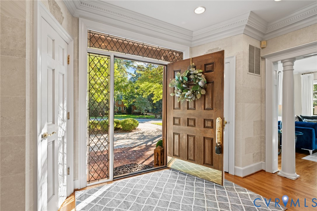 Foyer entrance featuring a solid wood paneled door, diamond-patterned leaded glass sidelight, stone-textured wall finishes, recessed lighting, and a columned entryway
