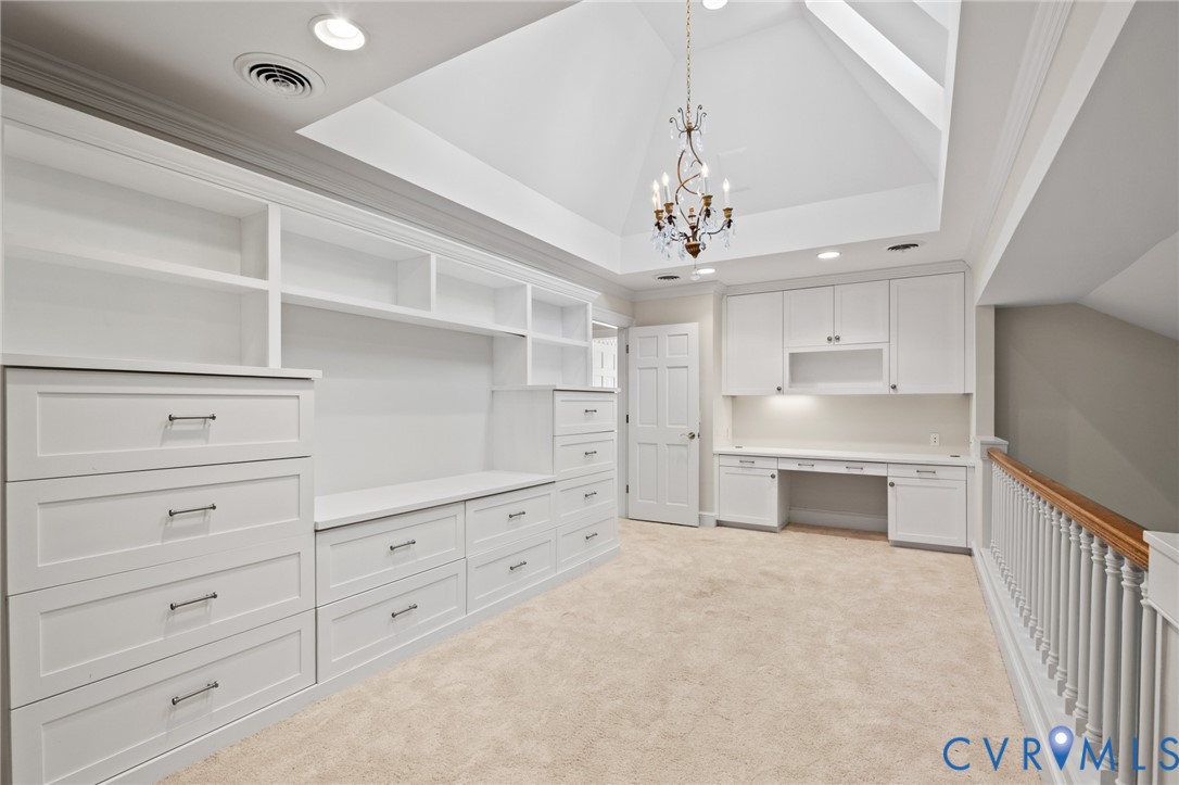 Vaulted ceiling featuring a decorative chandelier, extensive custom built-in white cabinetry, integrated desk workspace, and a classic wood-capped railing