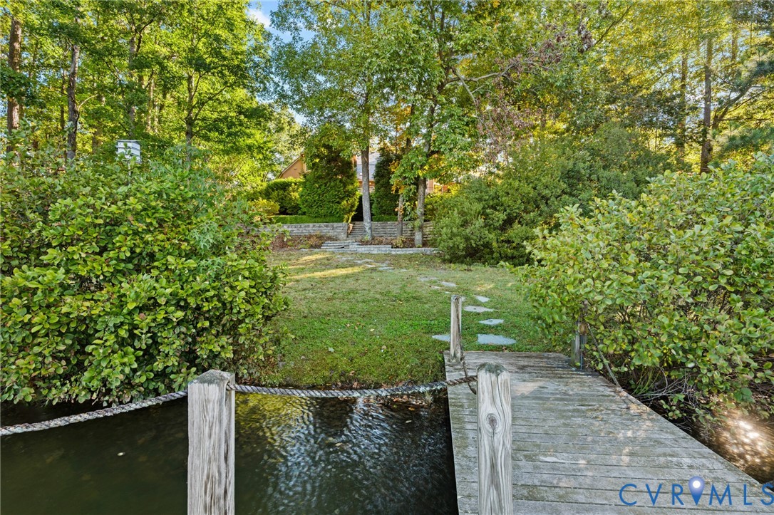 Waterfront property featuring a wooden dock, stone pathway, grass lawn, and mature trees