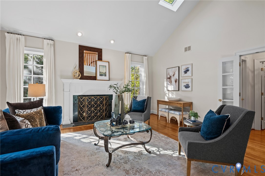 Vaulted ceiling with skylight, wood-finish flooring, and a fireplace featuring a white mantel and dark stone surround