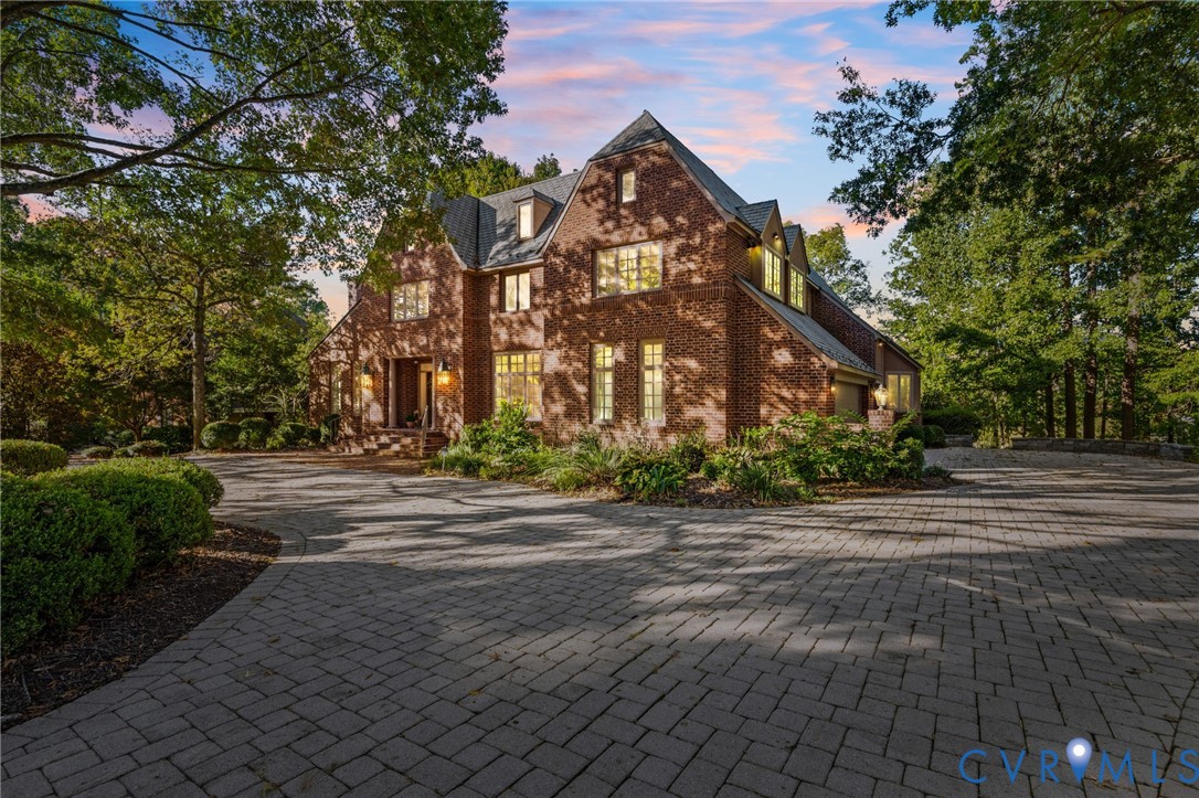 Multi-story brick exterior featuring a steeply pitched roof, gabled dormers, multi-pane windows, and a paved stone driveway